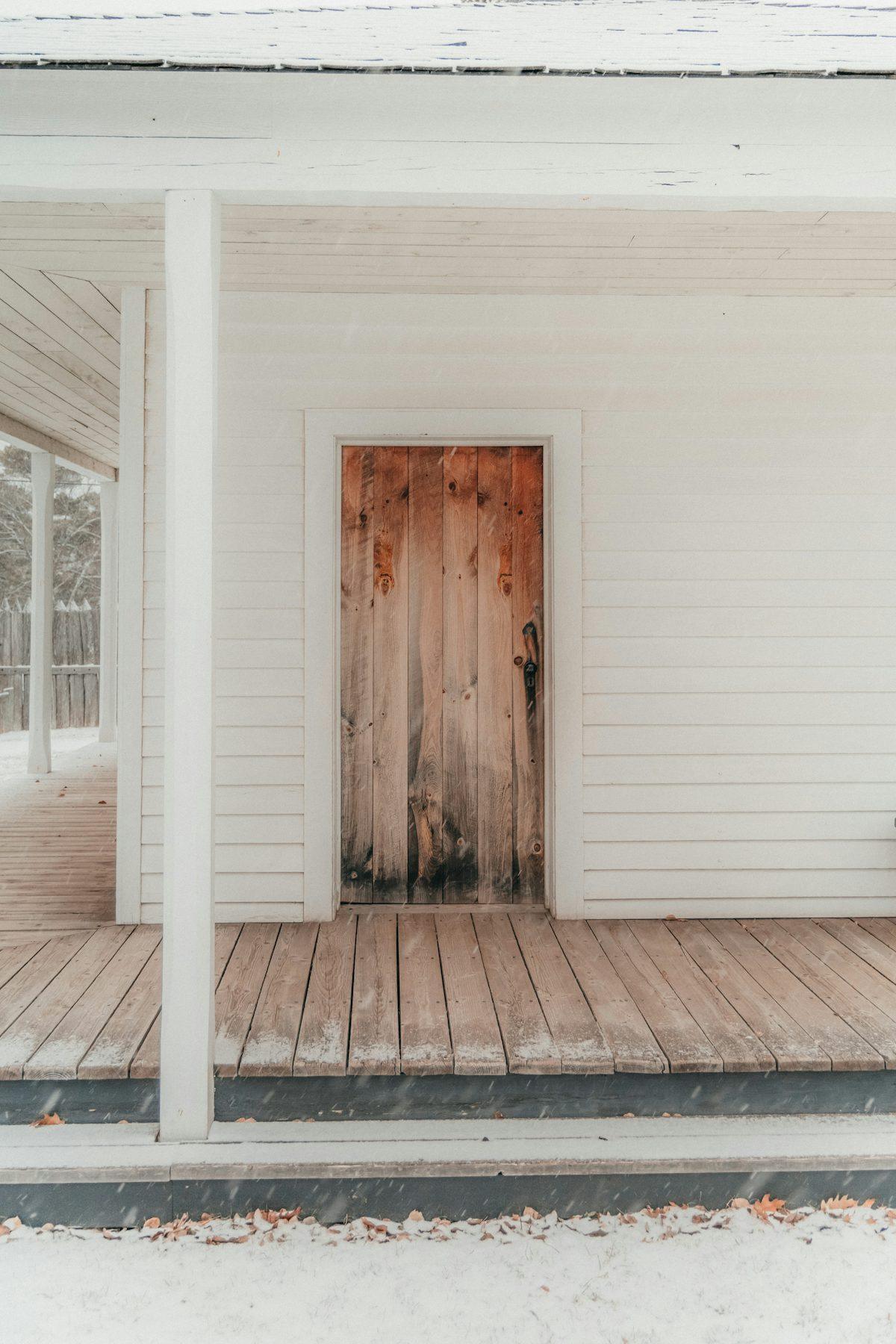 A white house with a wood door and a porch in daylight.